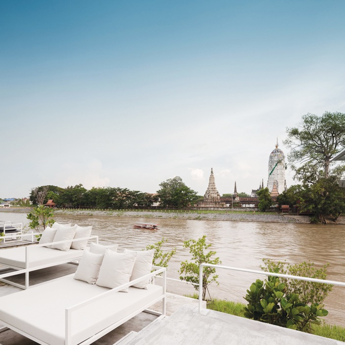 Khu vực thư giãn và nhà hàng ngoài trời, bên kia bờ sông là những đền tháp cổ kính của cố đô Ayutthaya với ngôi đền thiêng Putthai Sawan (cao, bên phải)